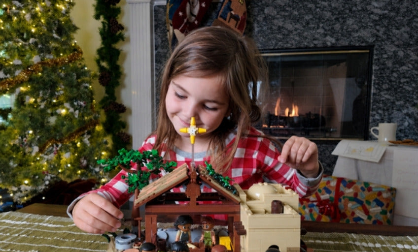 A girl building the Nativity set by the Christmas tree